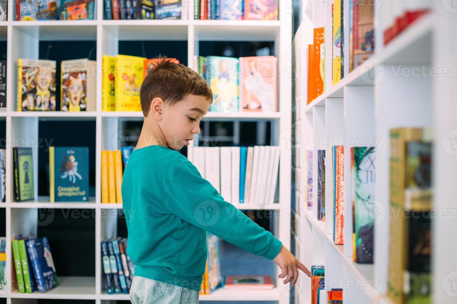 Ein kleiner Junge greift in der Buchhandlung nach einem Regal mit Kinderbüchern. foto