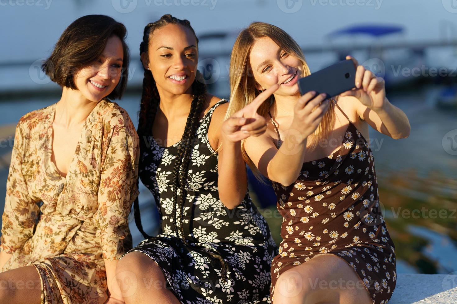 positive vielfältige frauen, die selfie in der nähe des flusses machen foto