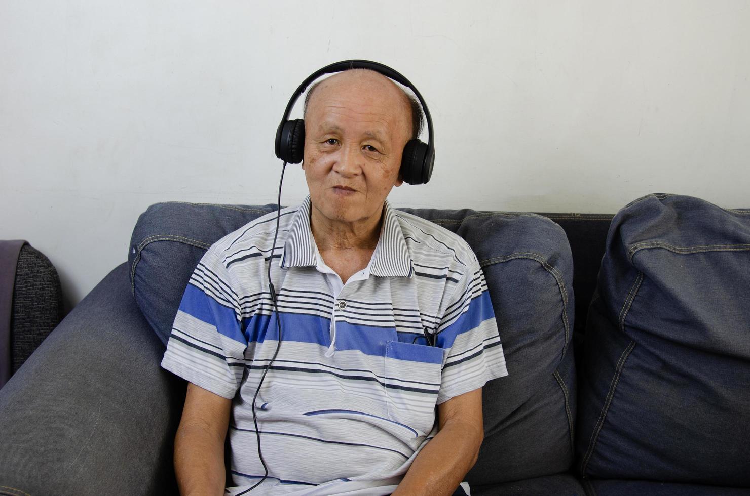 älterer mann, der musik mit kopfhörern auf dem sofa hört. foto