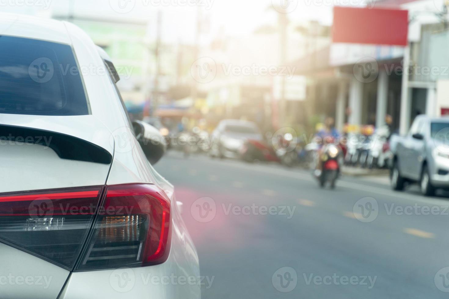 Rückseite des Autos und Rücklicht des weißen Autos auf der Asphaltstraße. mit Bremslicht. verschwommene Umgebung der Stadt, andere Autos und Motorräder. foto