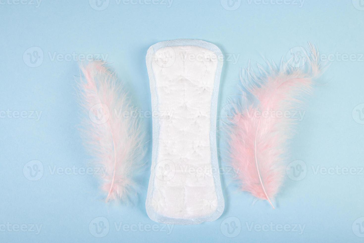 Damenbinde und Feder auf blauem Hintergrund. Produkte für die weibliche Menstruationshygiene. foto