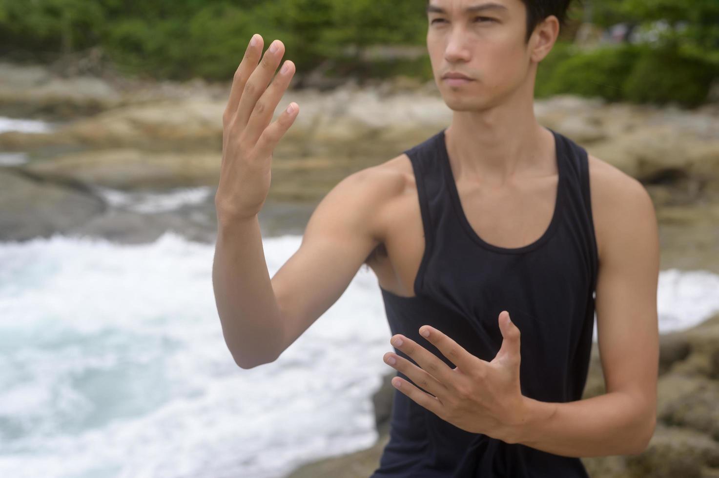 junger mann in sportbekleidung, der kampfkunst, qigong, tai chi auf dem felsen am meer, gesundheits- und meditationskonzept macht foto