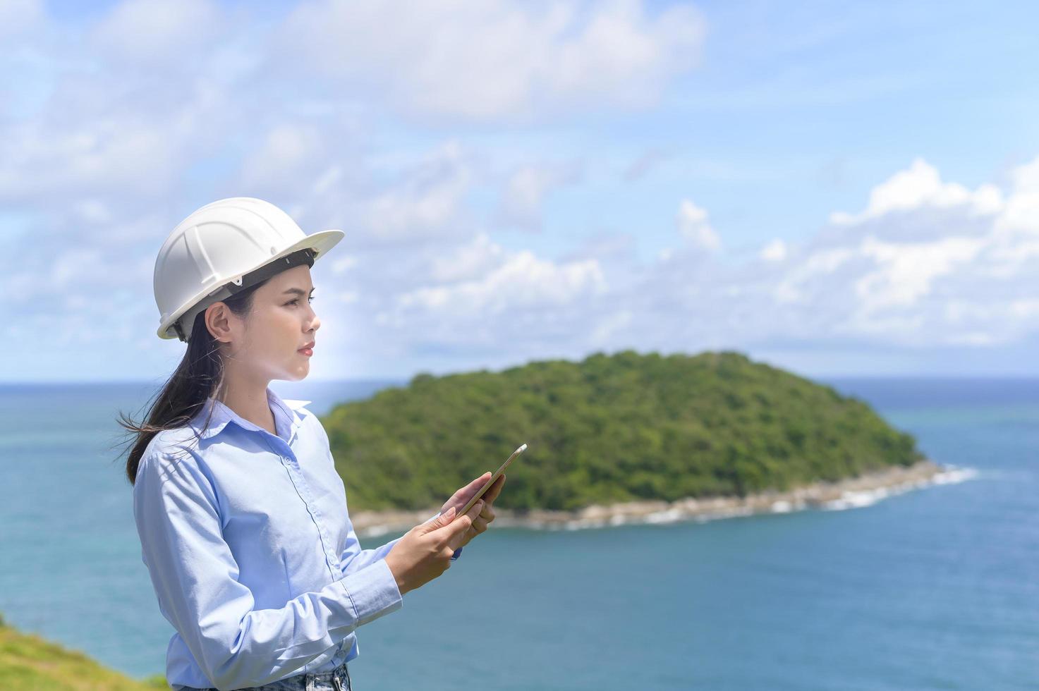 Ingenieurin, die am Meer arbeitet und einen Schutzhelm trägt foto