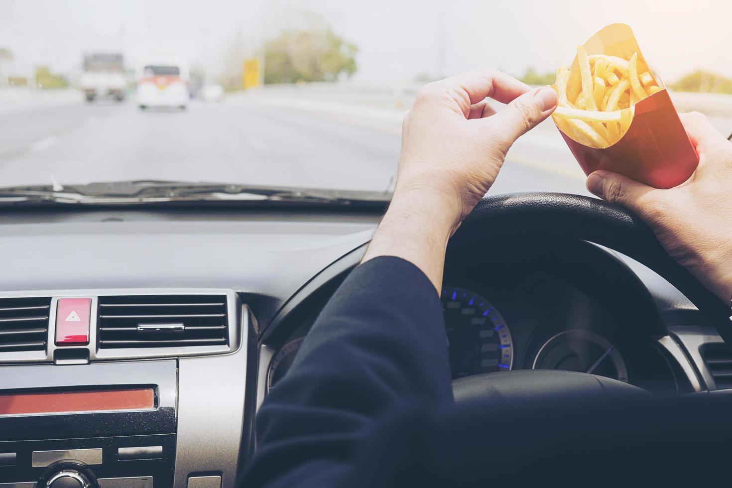 geschäftsmann, der pommes frites isst und gefährlich auto fährt foto