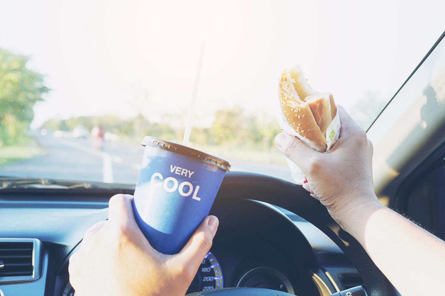 Mann isst gefährlich Hotdog und kaltes Getränk beim Autofahren foto