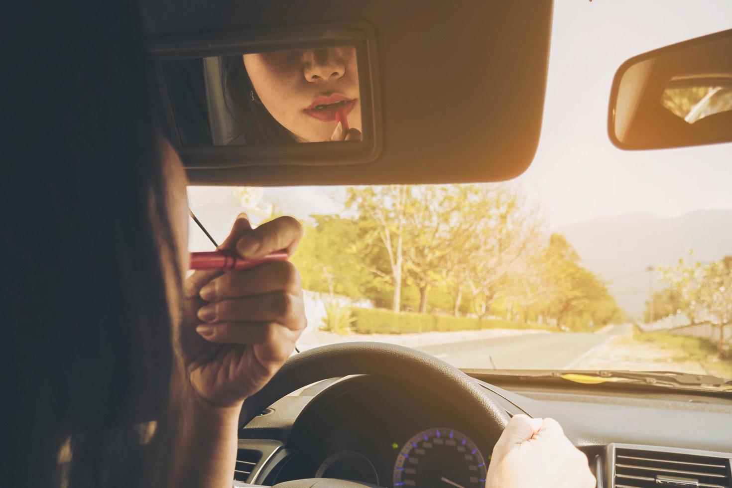 Frau, die ihr Gesicht mit Lippenstift schminkt, während sie Auto fährt, unsicheres Verhalten foto