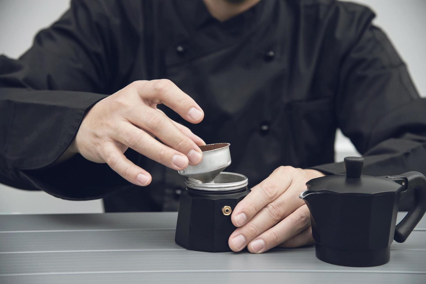 Der asiatische Barista verwendet eine Handkaffeemühle, um heißen Kaffee zuzubereiten foto