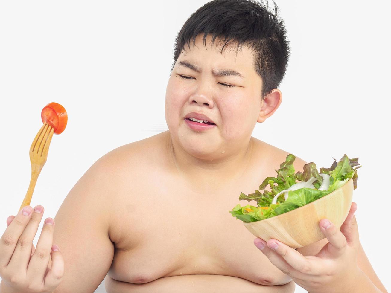 Ein dicker Junge hasst es, Gemüsesalat zu essen foto