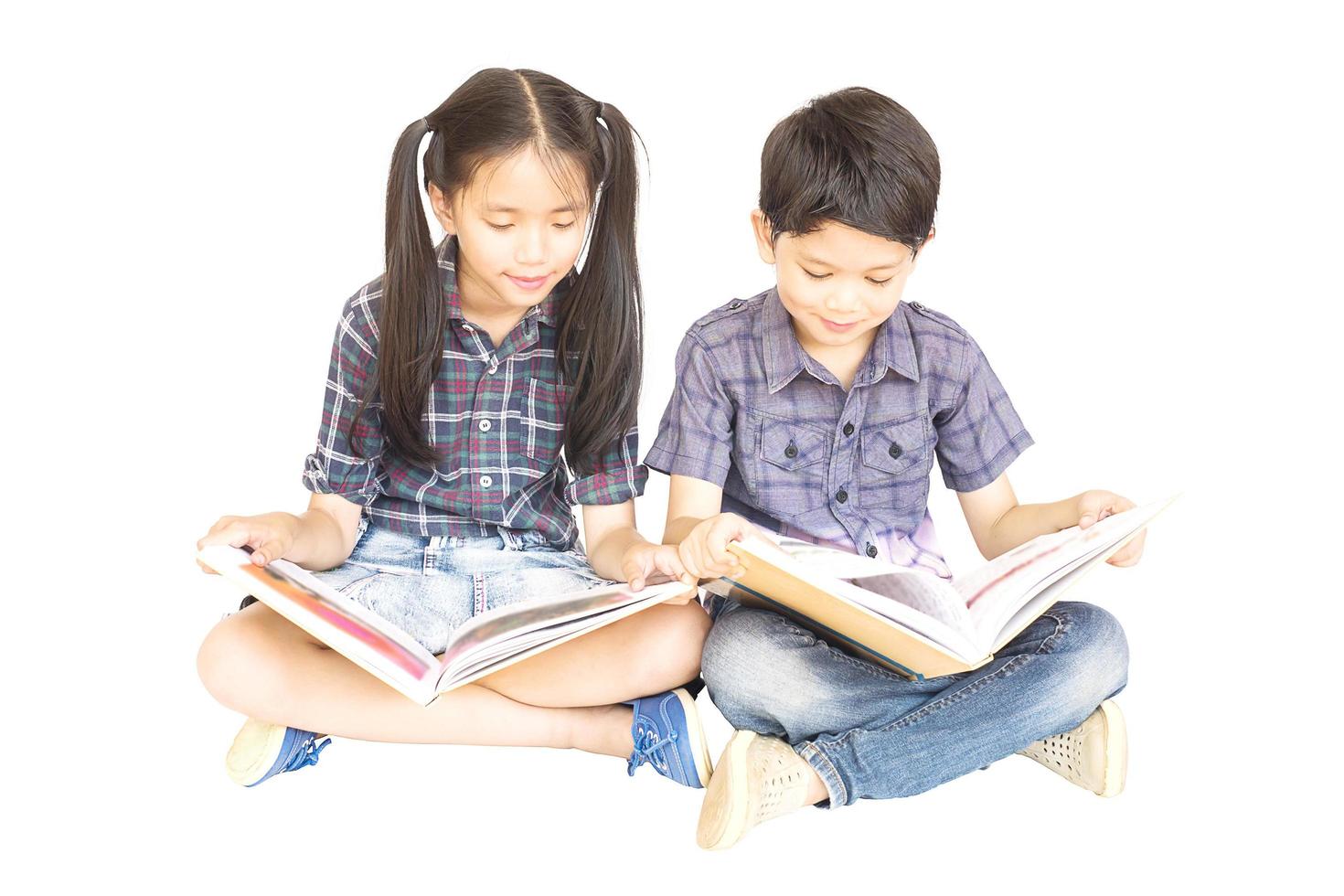 10 und 7 Jahre asiatisches Schulmädchen und -junge, die glücklich zusammensitzen und Buch isoliert über Weiß lesen foto