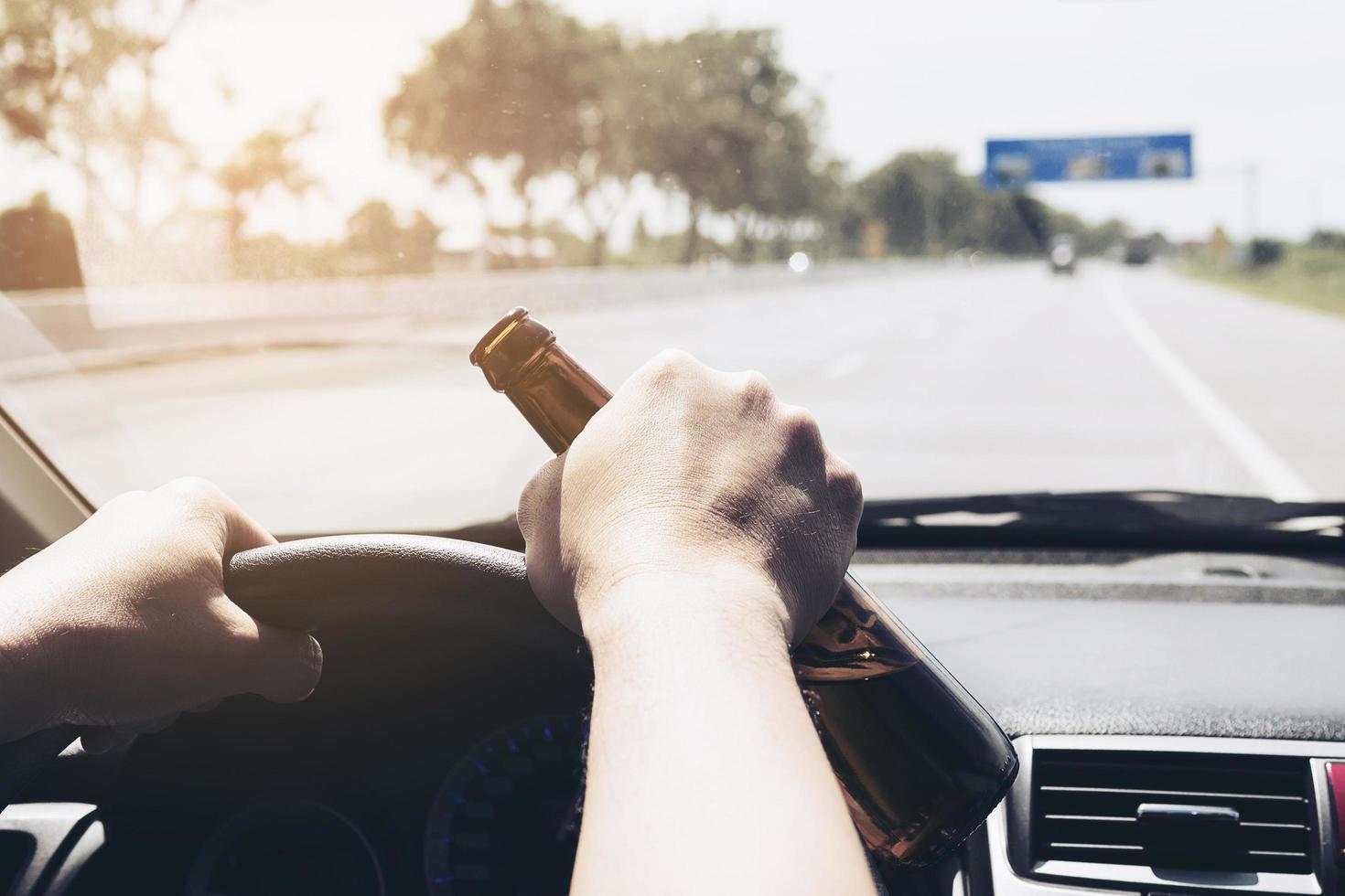 Mann hält Bierflasche beim Autofahren foto