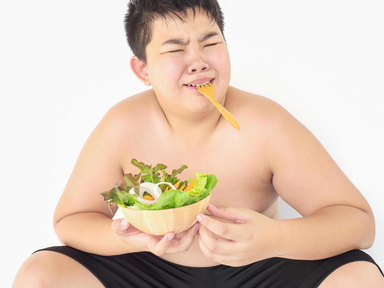 Ein dicker Junge hasst es, Gemüsesalat zu essen foto