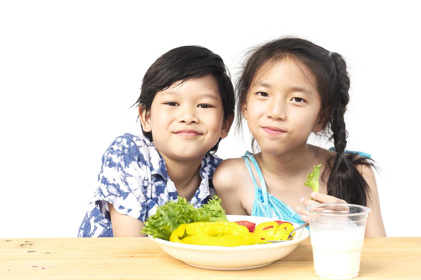 asiatischer reizender junge, der zeigt, genießen ausdruck mit frischem buntem gemüse und glas milch lokalisiert über weißem hintergrund foto