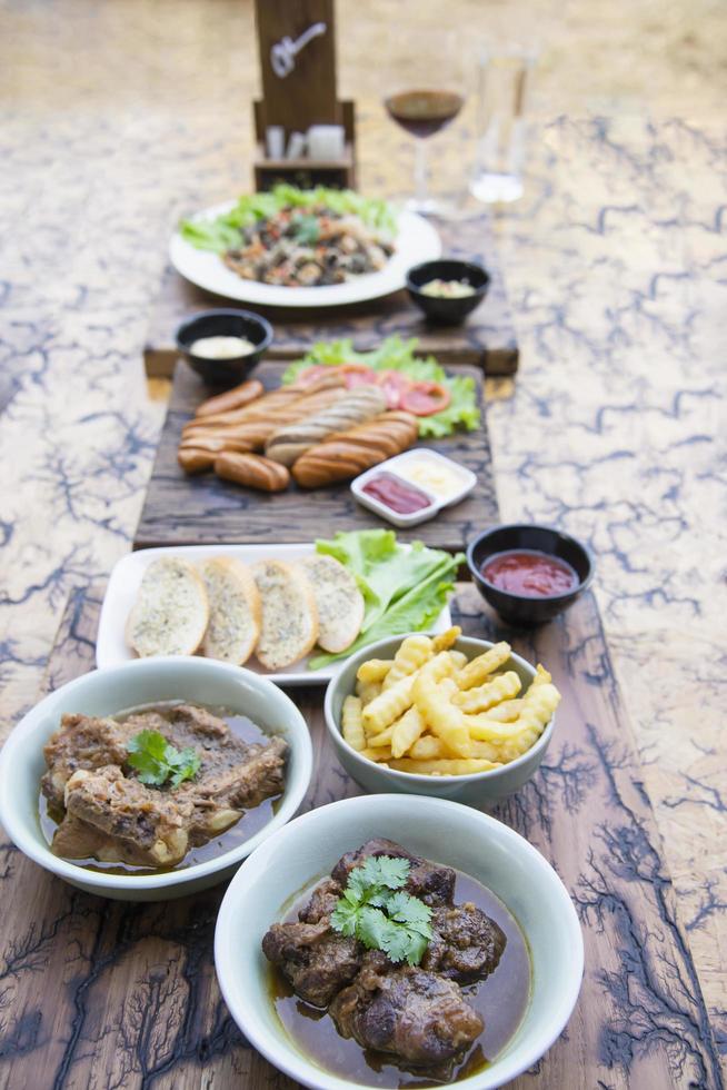 rindfleisch- und schweineintopf mit pommes frites und anderen lebensmittelrezepten auf holztisch, essensmahlzeiten, die zum essen bereit sind foto