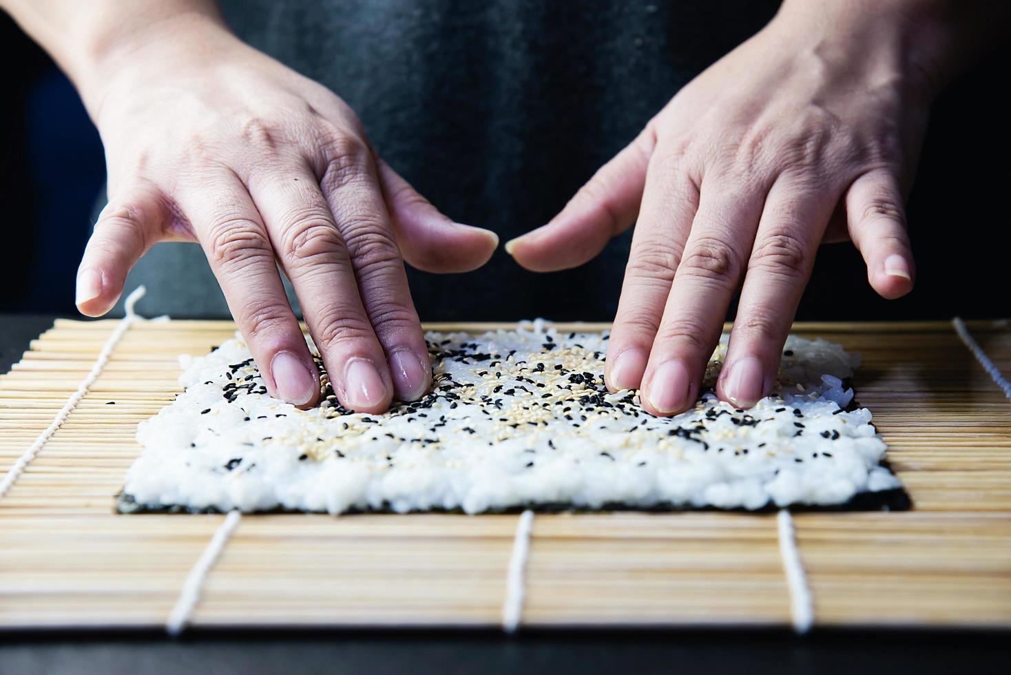 koch, der sushi roll über schwarzem tischhintergrund zubereitet - leute mit lieblingsgericht japanisches lebensmittelkonzept foto