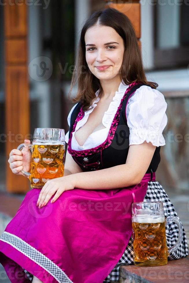 sexy russische frau im bayerischen kleid, das bierkrüge hält. foto