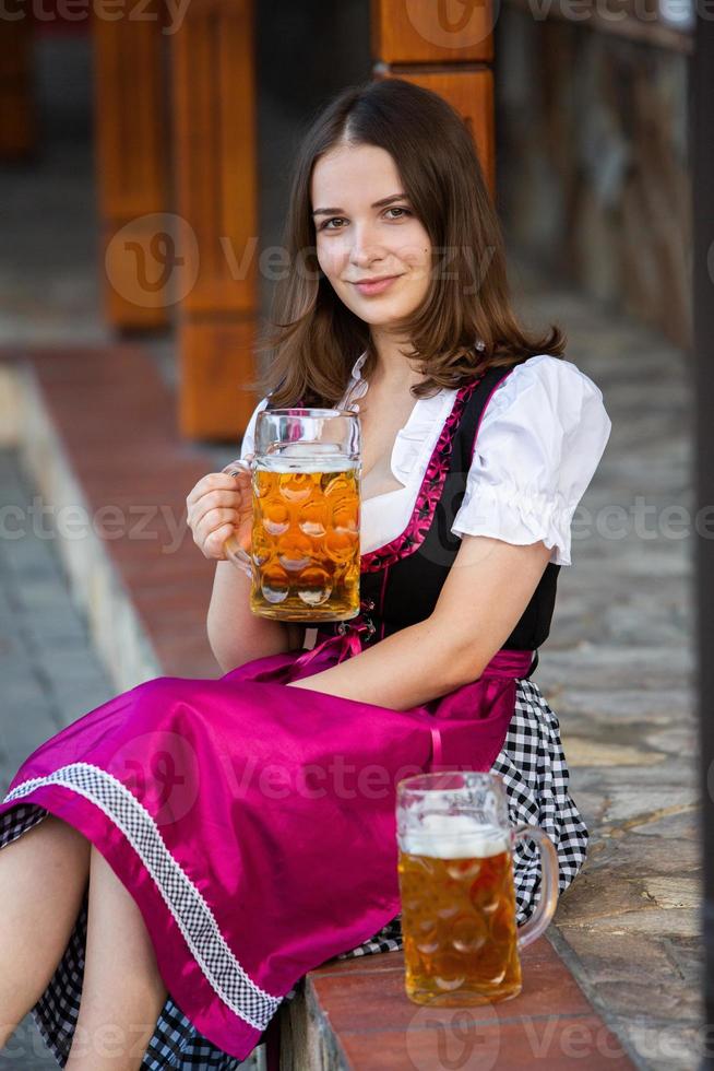 sexy russische frau im bayerischen kleid, das bierkrüge hält. foto