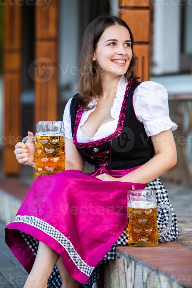 sexy russische frau im bayerischen kleid, das bierkrüge hält. foto