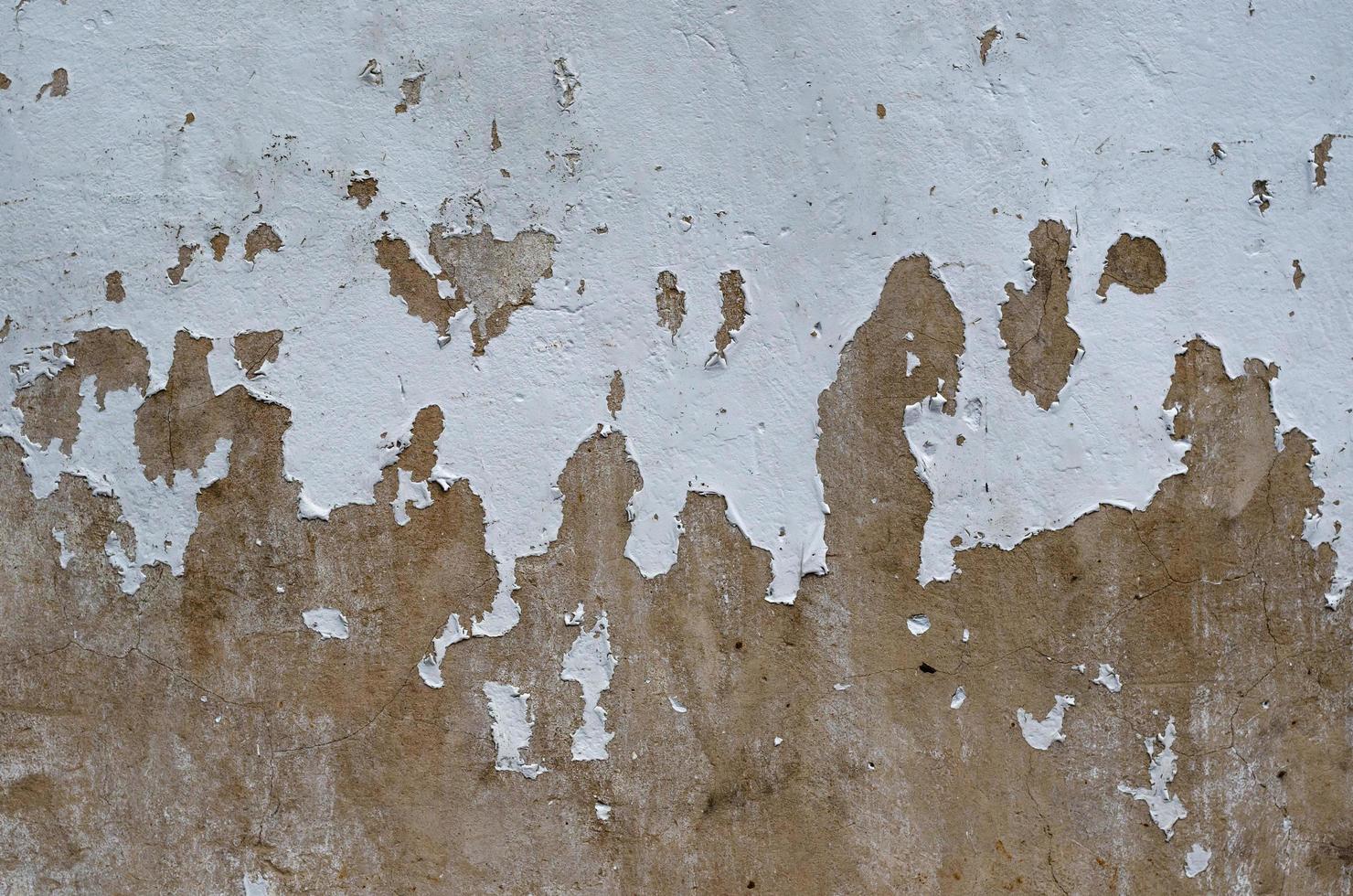 alt und abgezogen von weißer malerei, die auf der braunen zementwandoberfläche gerissen ist foto
