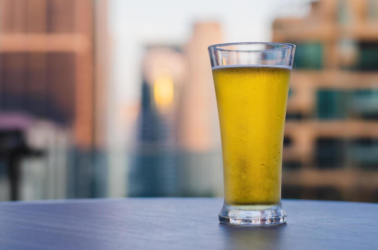 Ein Glas Bier wird in der Bar auf dem Dach mit verschwommenem Stadthintergrund auf den Tisch gestellt. foto
