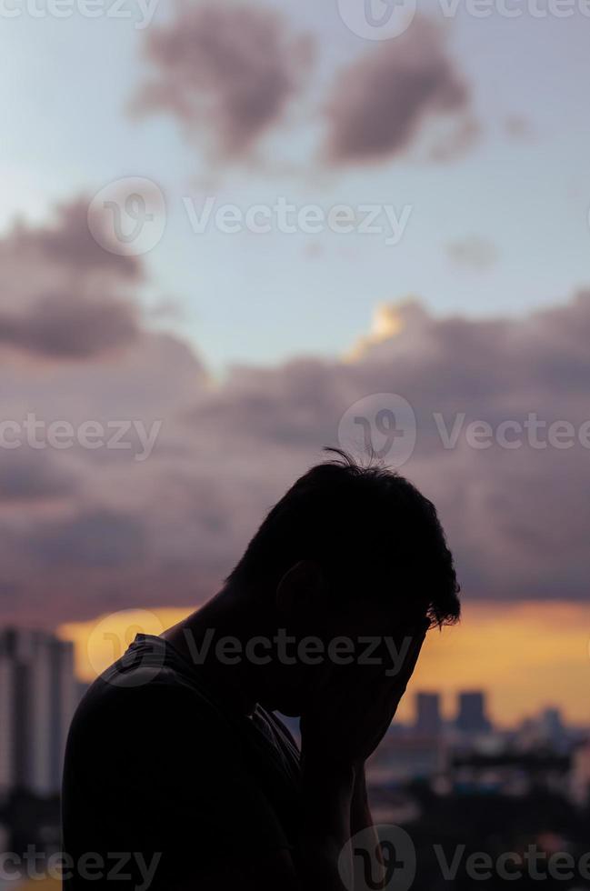 Silhouette eines weinenden depressiven Mannes mit Wolkenhimmel und Stadthintergrund. foto