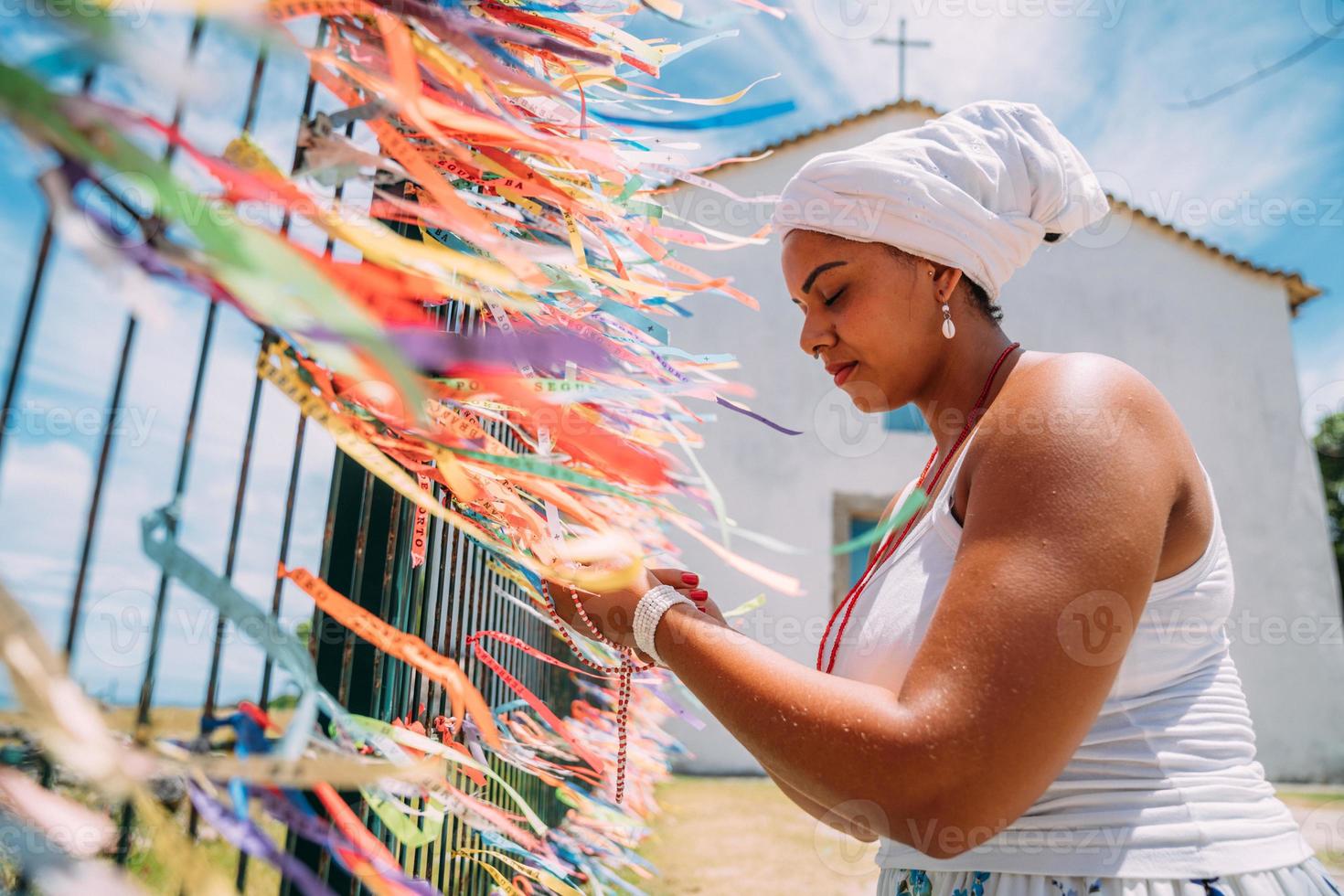 Brasilianerin, gekleidet in der traditionellen bahianischen Tracht der Umbanda-Religion, die ein Gebet spricht. konzentrieren sie sich auf farbige bänder religiöser versprechen in hingabe an senhor do bonfim in bahia, brasilien foto