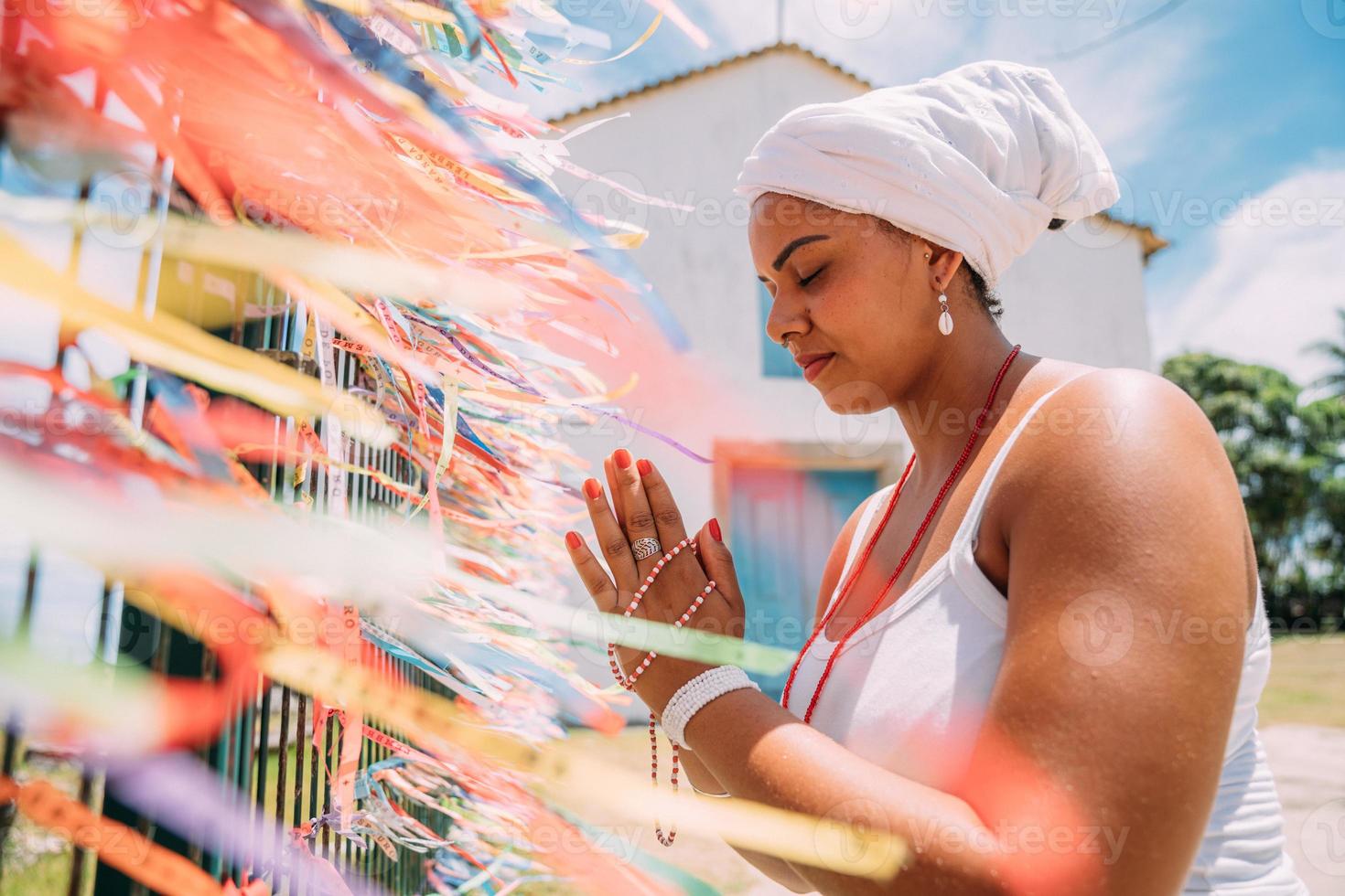 Brasilianerin, gekleidet in der traditionellen bahianischen Tracht der Umbanda-Religion, die ein Gebet spricht. konzentrieren sie sich auf farbige bänder religiöser versprechen in hingabe an senhor do bonfim in bahia, brasilien foto