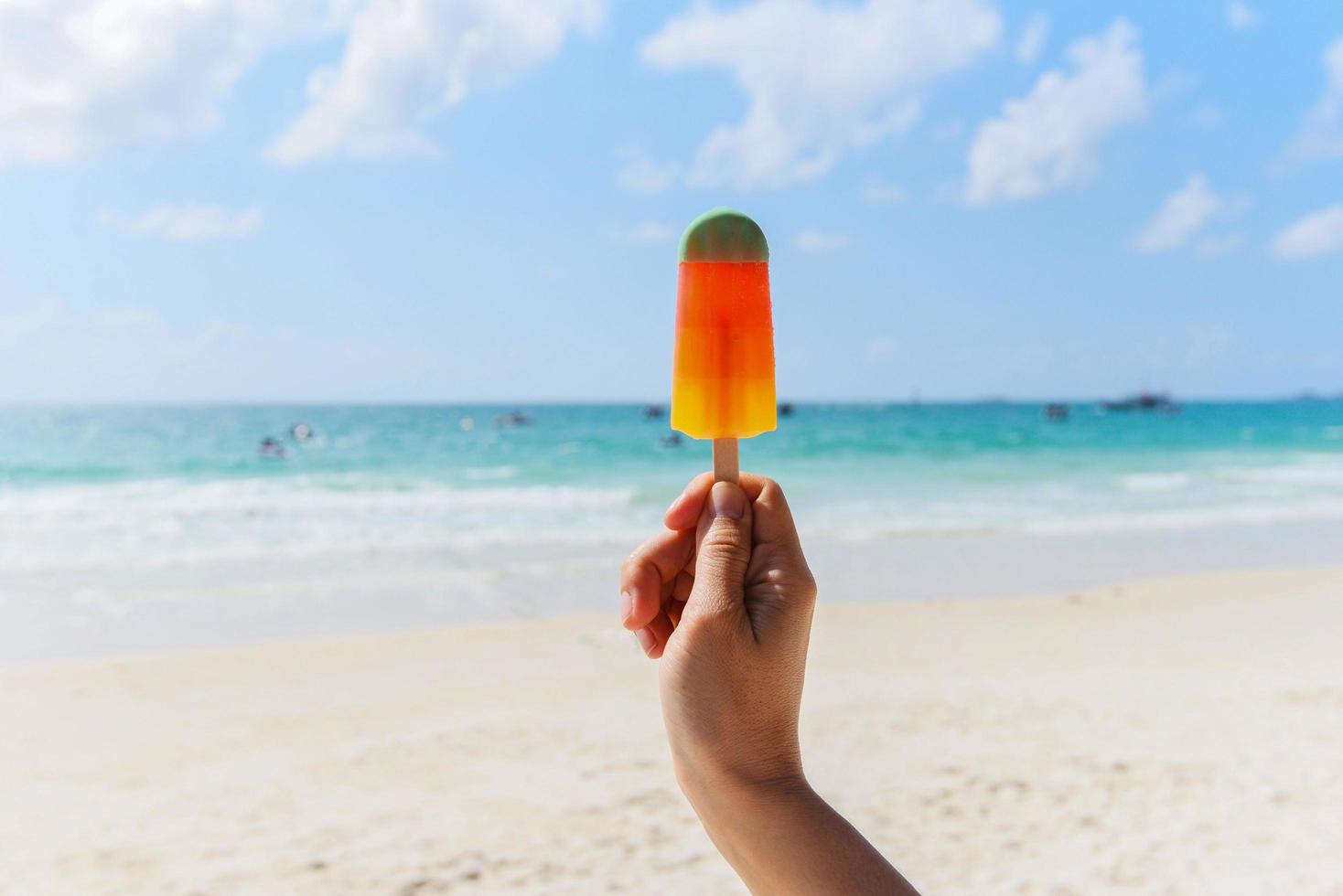 Eisstock in der Hand mit Meereshintergrund - bunte Eisfrucht am Strand bei heißem Wetter im Sommer Ozeanlandschaft Natururlaub im Freien foto