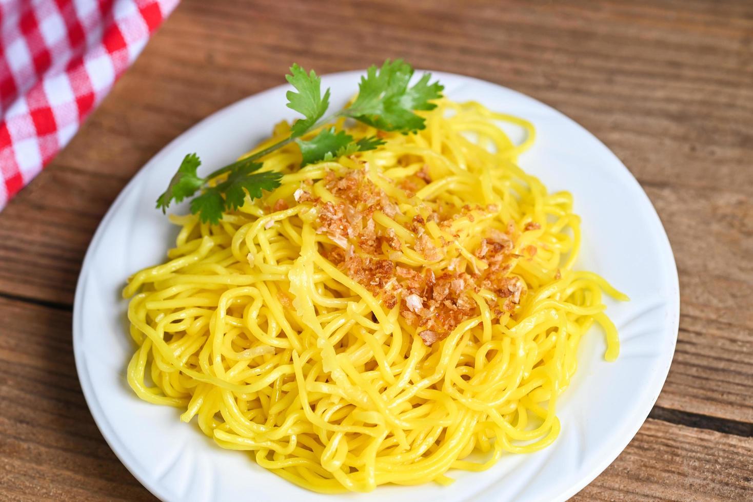 gelbe nudeln auf weißem teller und holzhintergrund, instant-nudeln gelbe nudeln reisnudeln essen mit gebratenem knoblauch und koriander foto