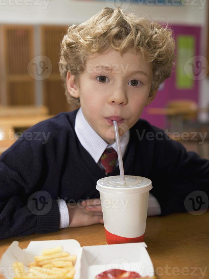 Junge sitzt mit Fast Food und trinkt durch Stroh foto