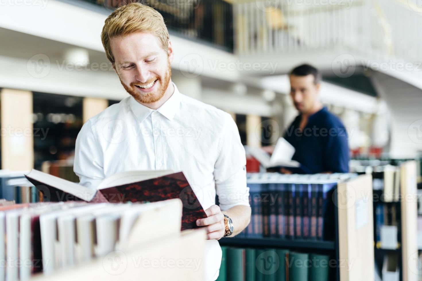 hübscher Student, der ein Buch in einer Bibliothek liest foto