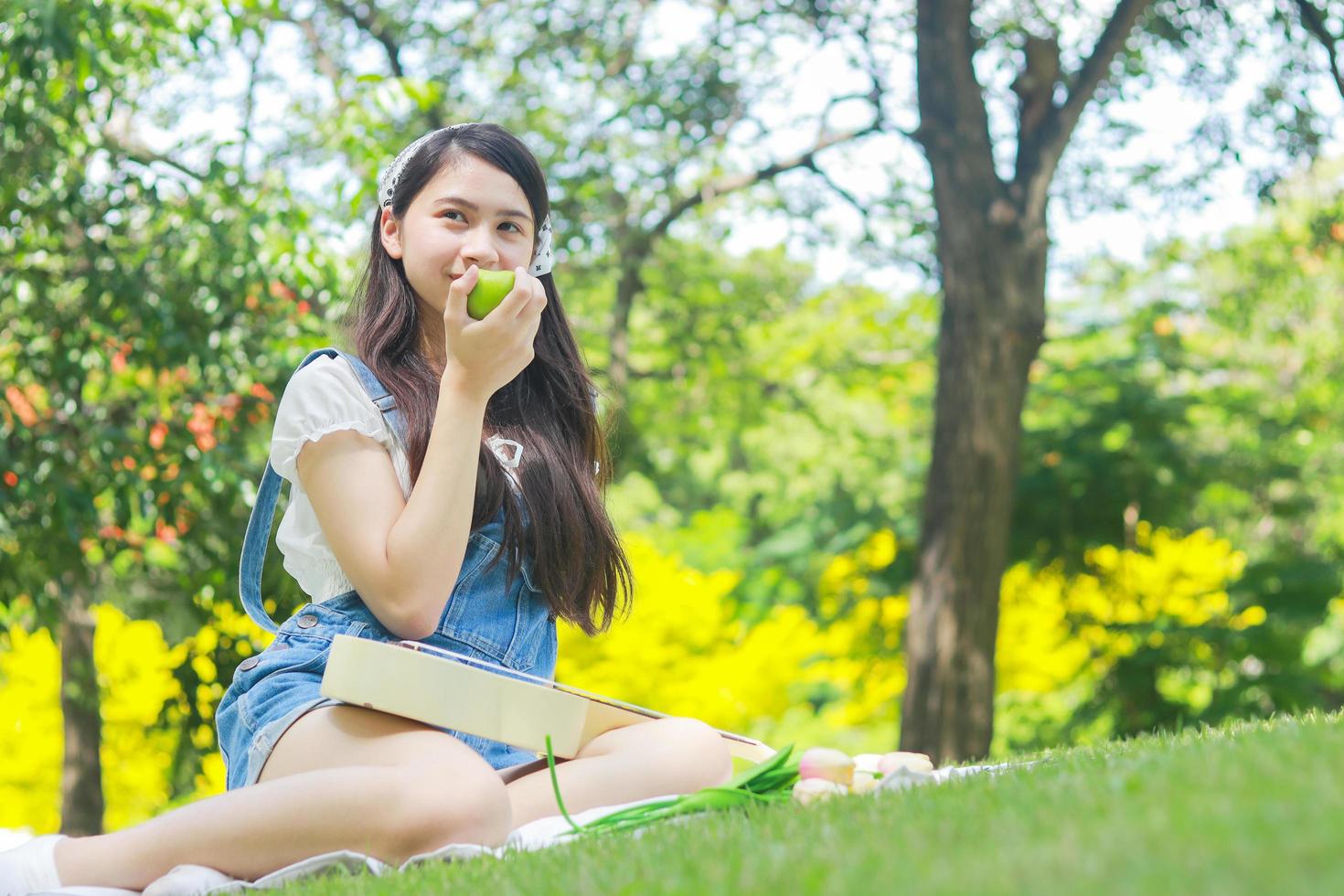 asiatische frau, die einen apfel hält, der sich entspannt und glücklich im park lächelt. foto