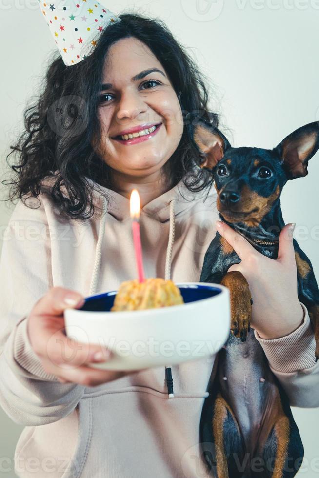 glückliches junges Mädchen, das ihrem Hund hausgemachten Kuchen gibt, drinnen foto