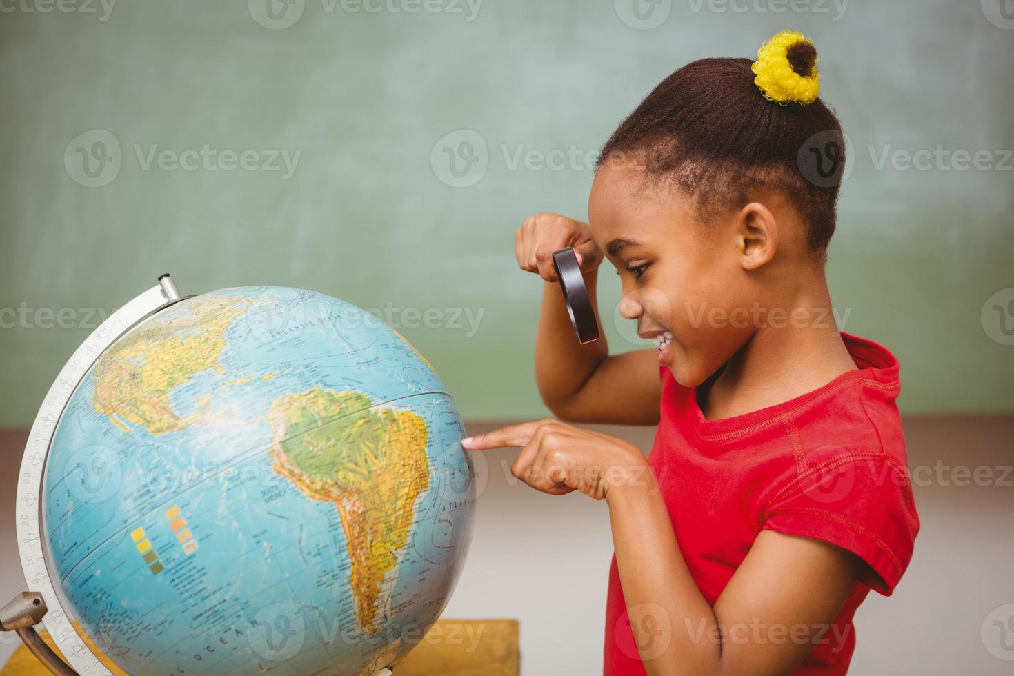 kleines Mädchen, das Globus durch Lupe betrachtet foto