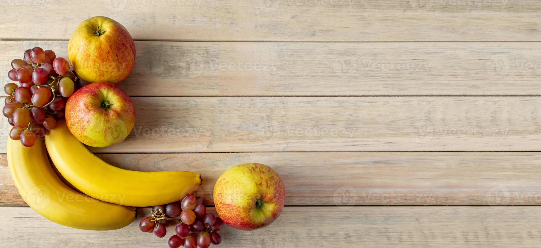 reife Früchte auf Holzhintergrund. Bananen, Äpfel und Weintrauben. Erntekonzept. foto