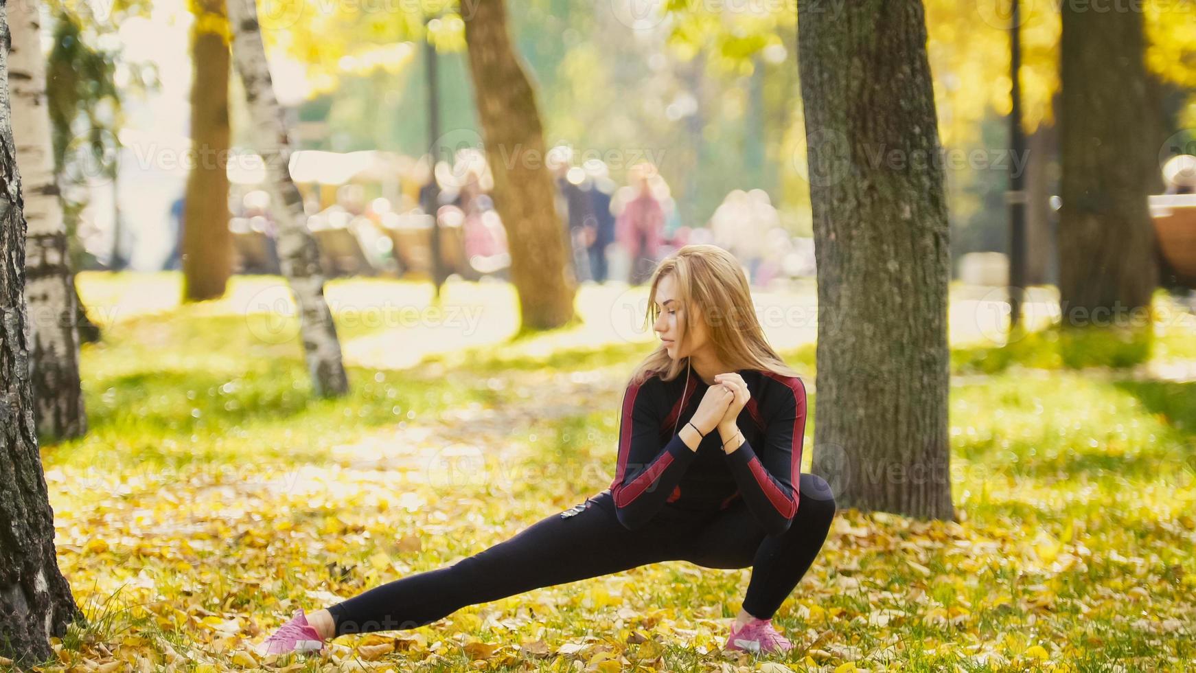 sexy attraktives weibliches blondes Bikini-Fitnessmodell, das sich im Herbstpark auf dem Boden ausdehnt, bedeckte gelbe Blätter - Beine Flexibilität - die rechte Seite foto