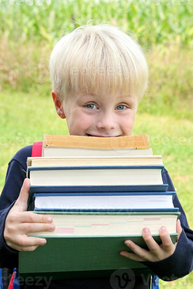 kleines Kind, das viele große schwere Schulbücher trägt foto