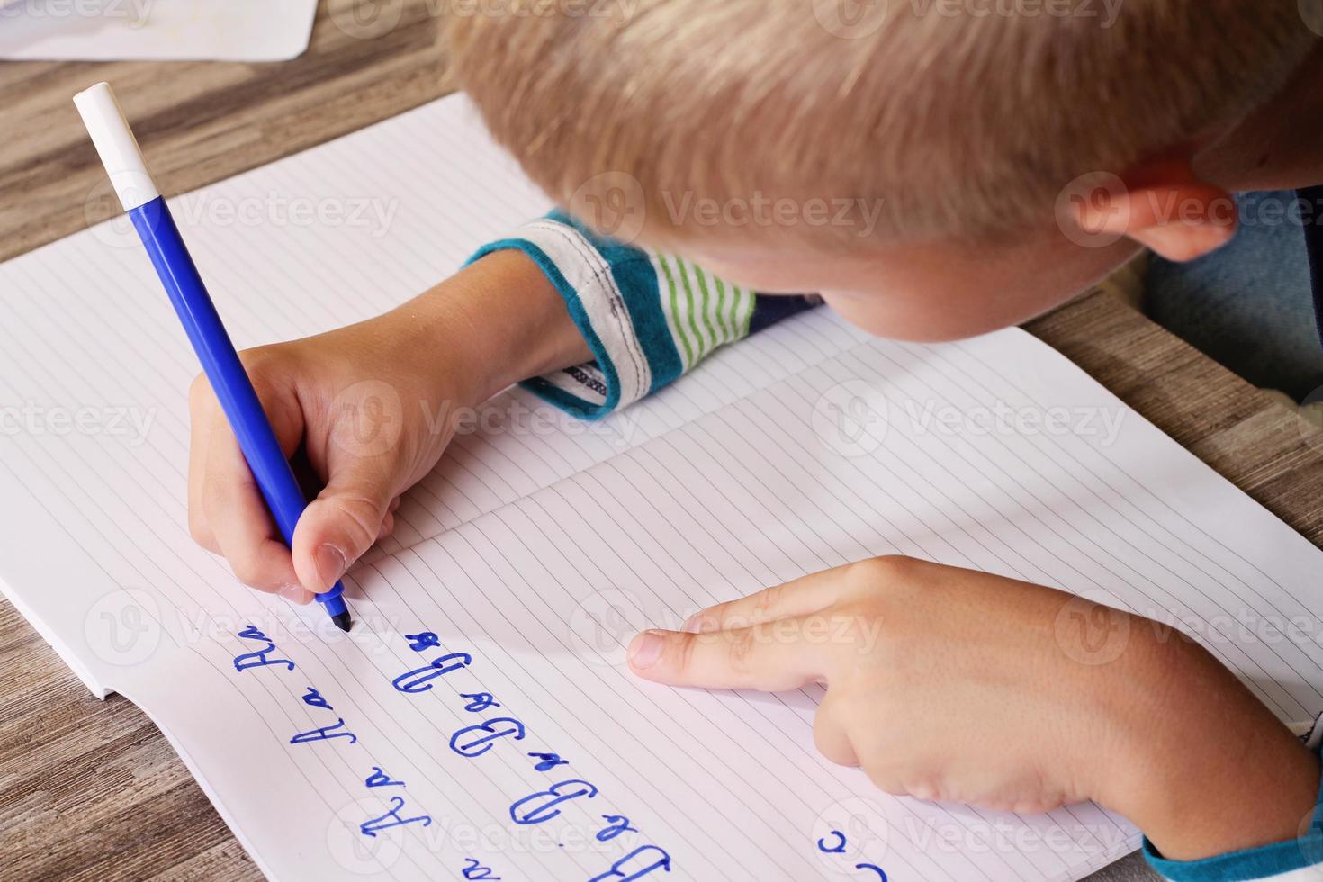 Schuljunge, der auf Papier schreibt, das Alphabet schreibt foto
