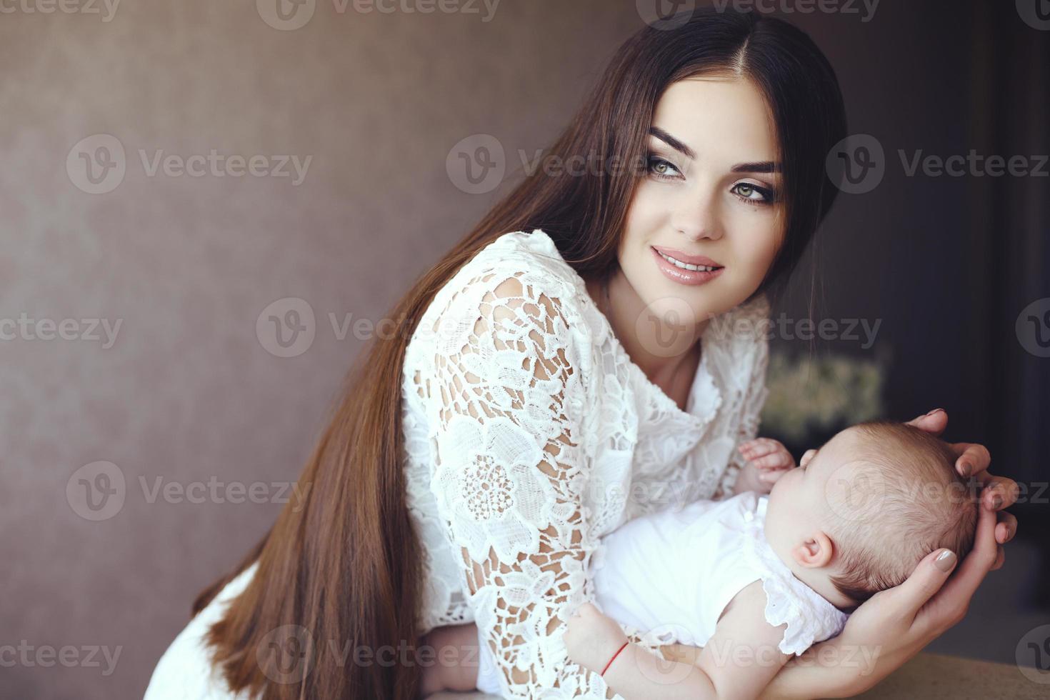 Mutter mit dunklen Haaren posiert mit ihrem kleinen entzückenden Baby foto