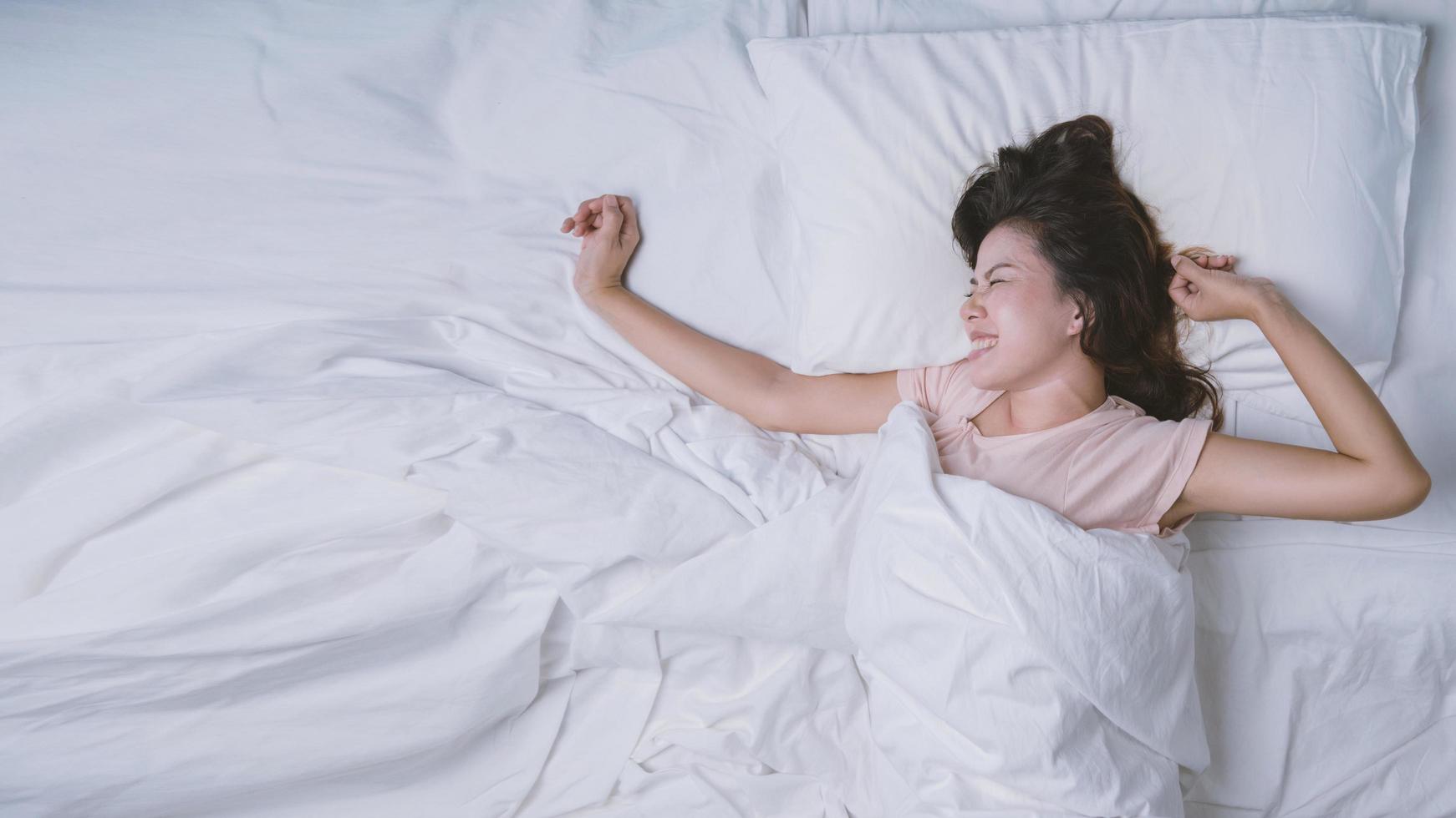 junge Frau, die gut im Bett schläft und weiches weißes Kissen umarmt. Teenager-Mädchen ruht. gutes Nachtschlafkonzept. Mädchen, das einen Pyjama trägt, schläft morgens auf einem Bett in einem weißen Raum. warmer Ton. foto