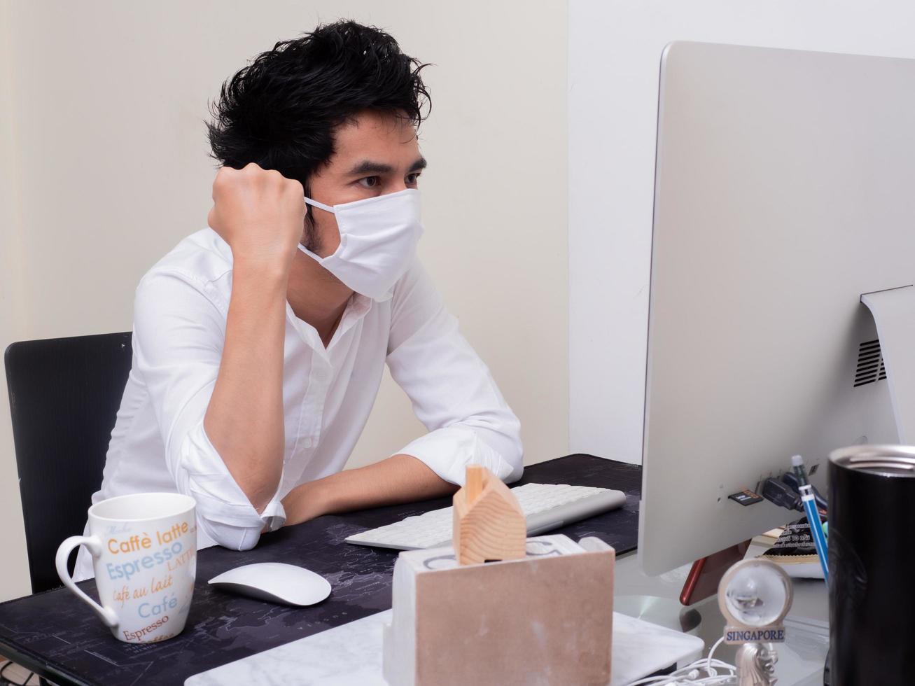 junger asiatischer junge mit gesichtsmaske, der während der coronavirus-pandemie am laptop arbeitet foto