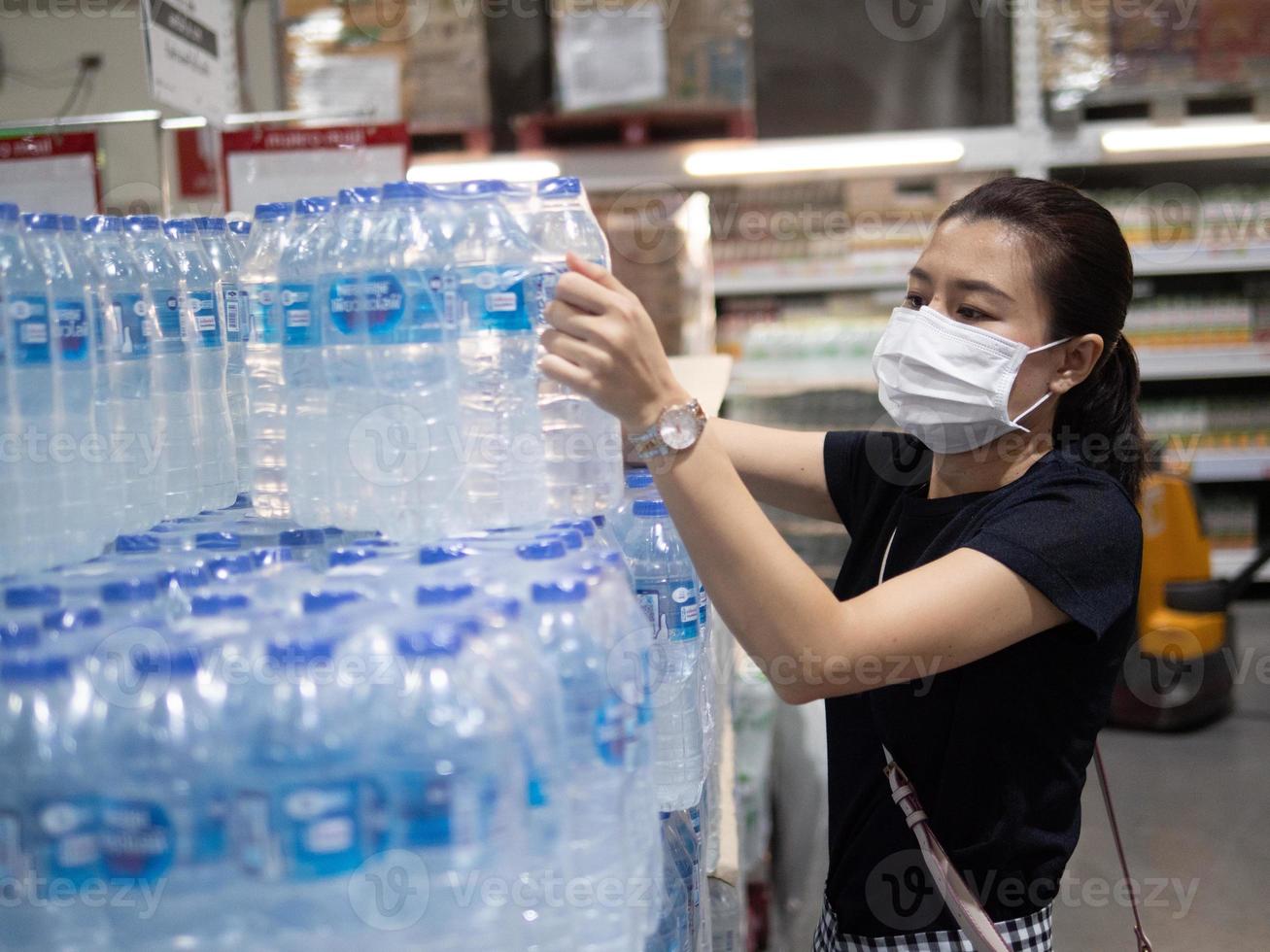 frau, die chirurgische maske und handschuhe trägt und trinkwasser im supermarkt kauft foto