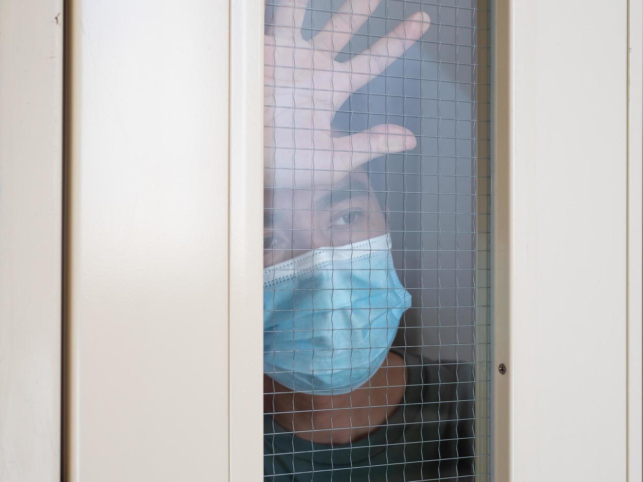 Einsamer Mann in medizinischer Maske, der durch das Fenster schaut. Isolierung zu Hause für Selbstquarantäne. konzept hausquarantäne, prävention covid-19. Ausbruchssituation des Coronavirus foto