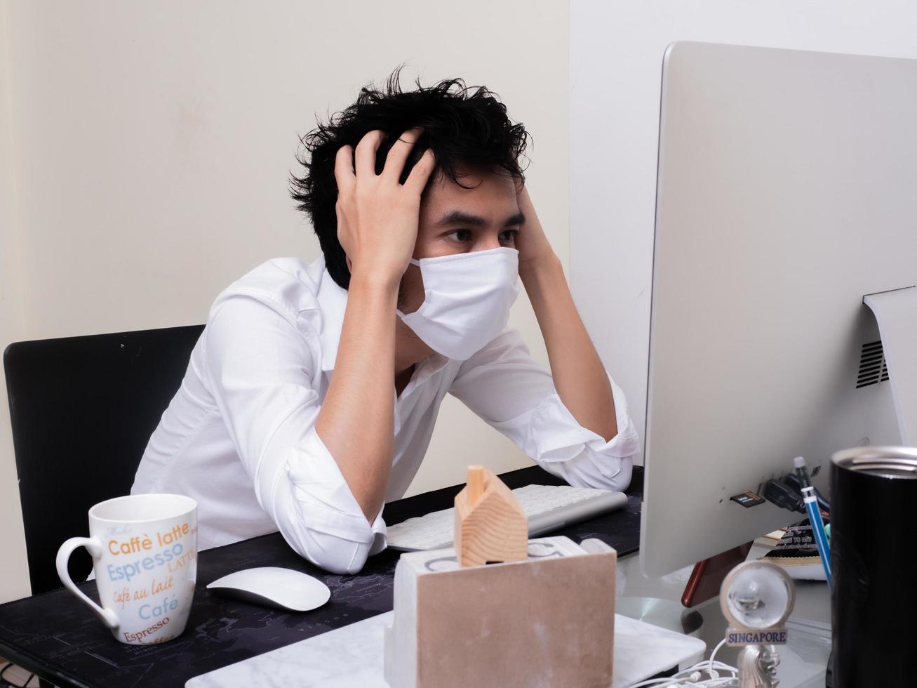 junger asiatischer junge mit gesichtsmaske, der während der coronavirus-pandemie am laptop arbeitet foto