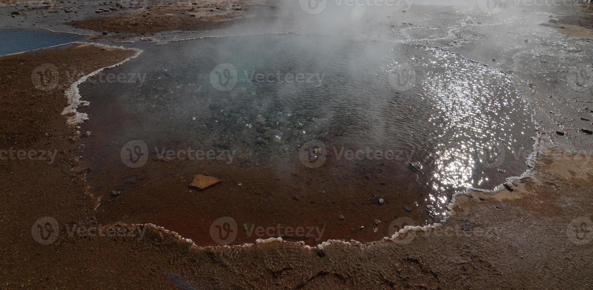 Kühler, dampfender Geysir in Island, umgeben von Mineralien foto