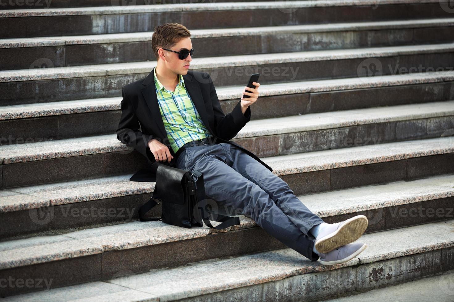 junger Mann mit einem Handy, das auf den Stufen sitzt foto