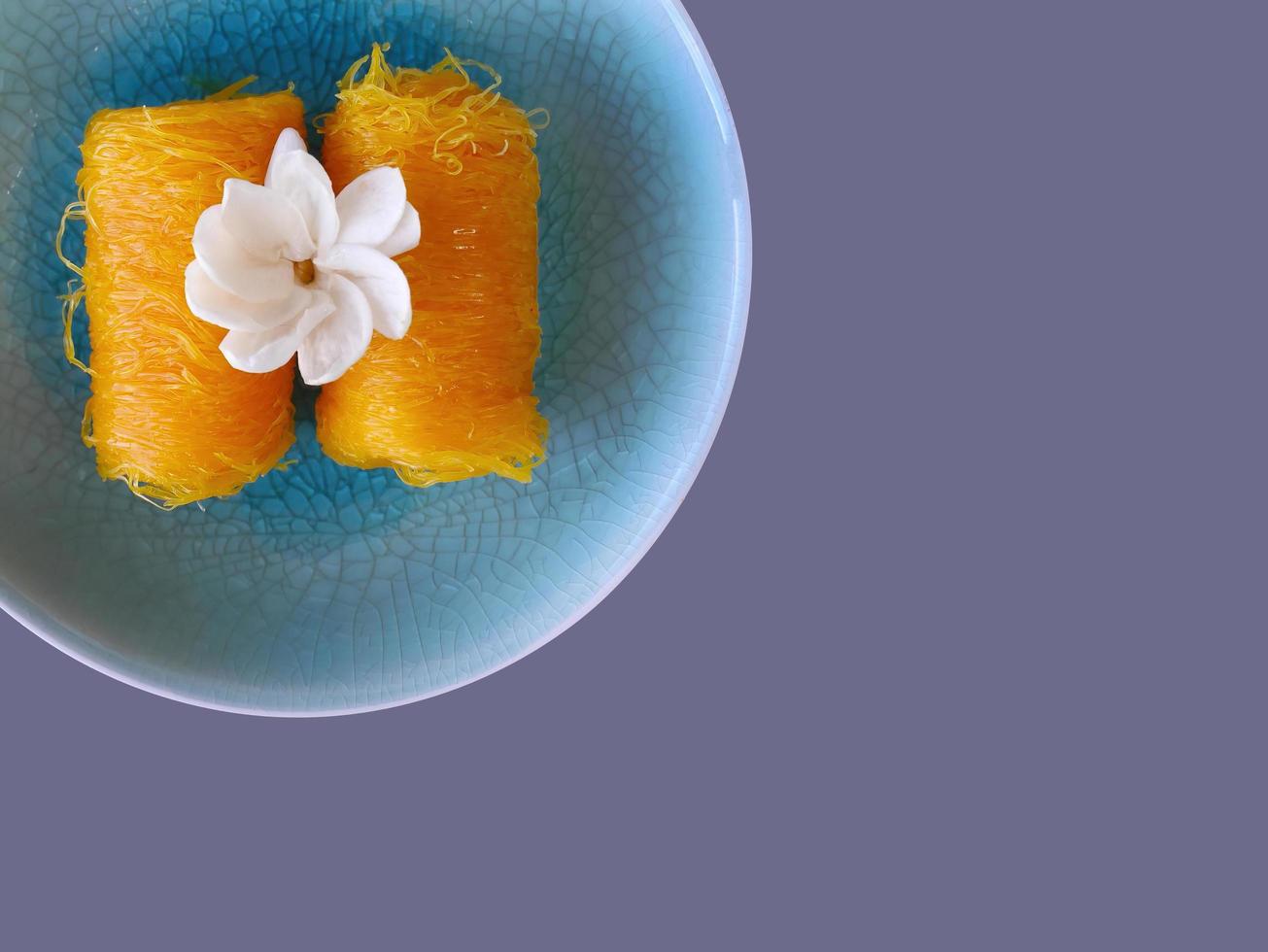 Ansicht von oben, Nahaufnahme von Fios de Ovos im thailändischen Stil, gerollter goldener Eigelbfaden, traditionelles Süßspeisendessert in blauer Seladonplatte, Kopierraum mit Beschneidungspfad foto