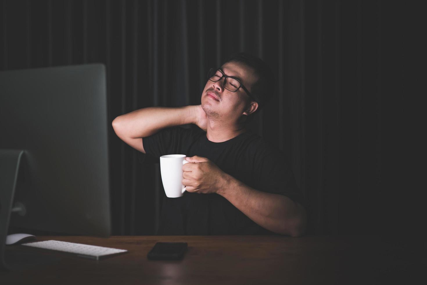 Nackenschmerzen oder müdes Konzept. mann, der seinen hals berührt, weil er nach langer arbeit am computer im dunklen raum zu hause schmerzen oder schmerzen hat foto