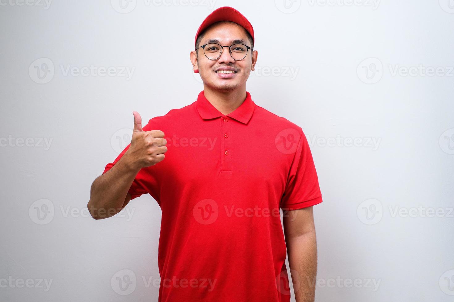 asiatischer lieferbote in roter uniform und kappe lächelnd und daumen nach oben isoliert zeigend foto