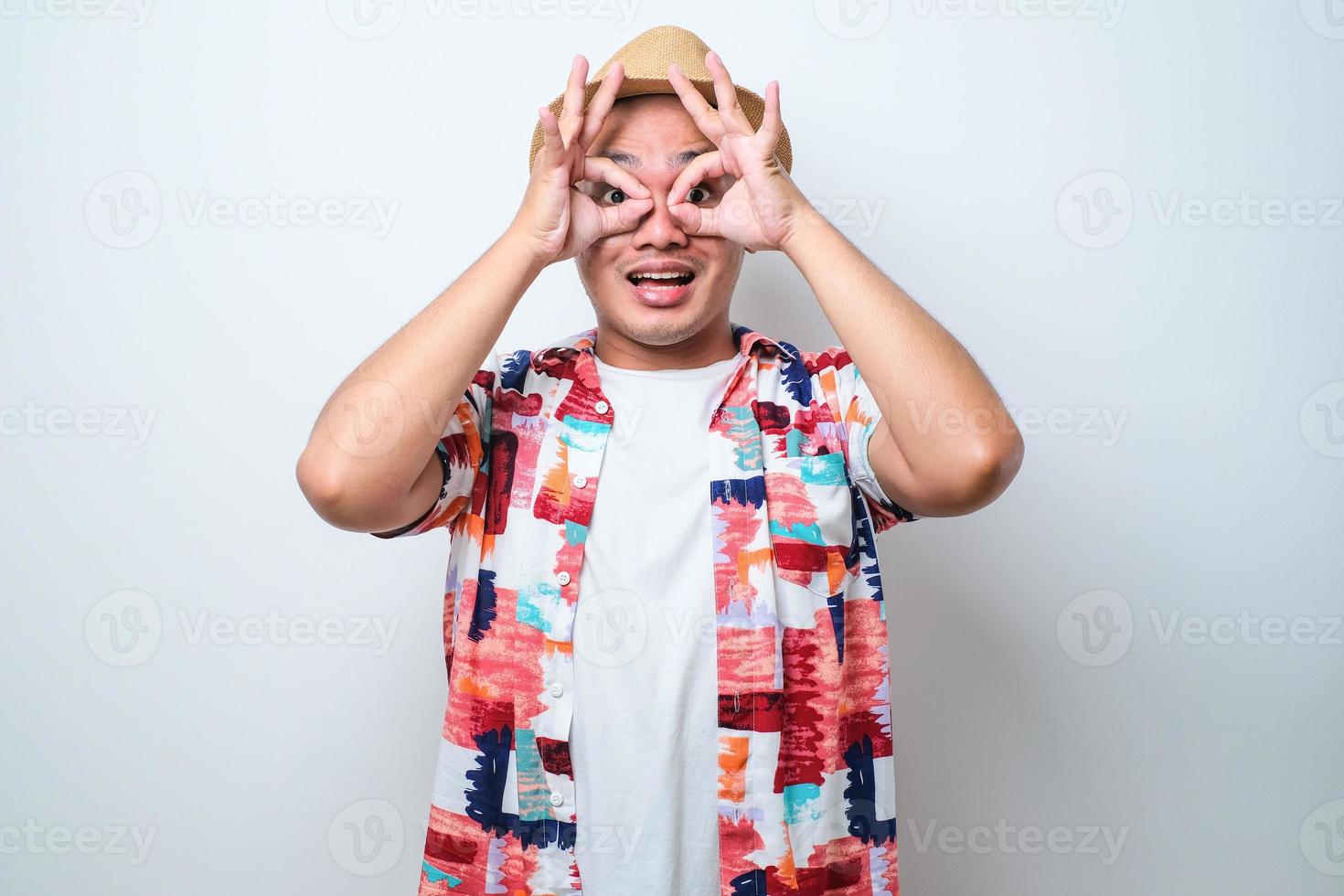 asiatischer mann, der ok geste macht, wie ein fernglas, das die zunge herausstreckt, augen, die durch finger schauen. foto