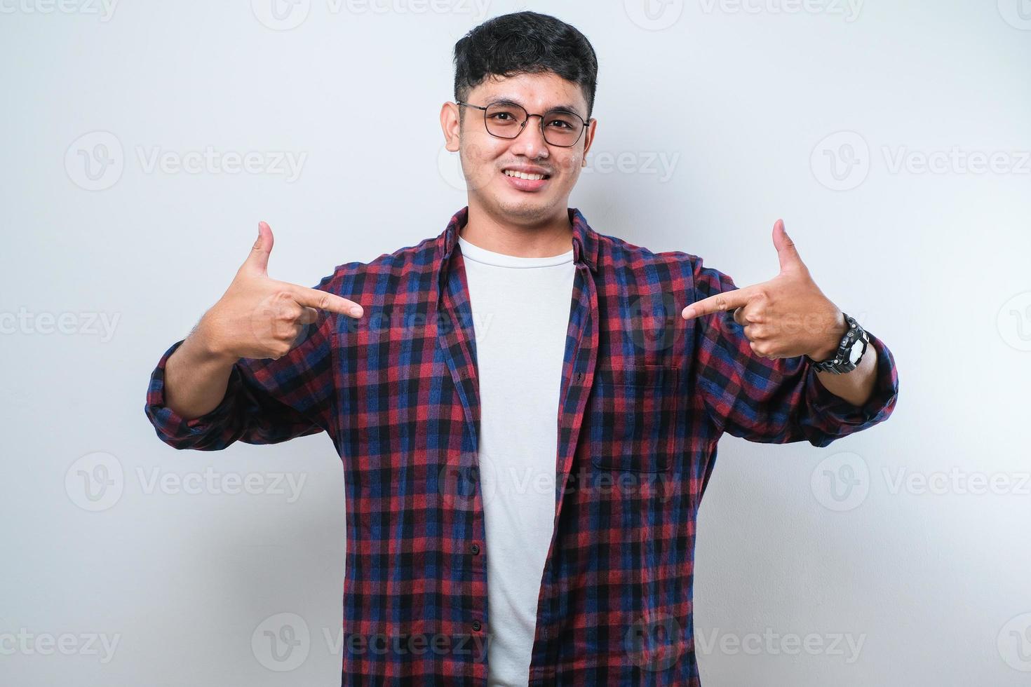 junger gutaussehender mann, der selbstbewusst mit einem lächeln im gesicht aussieht und sich mit den fingern stolz und glücklich zeigt foto